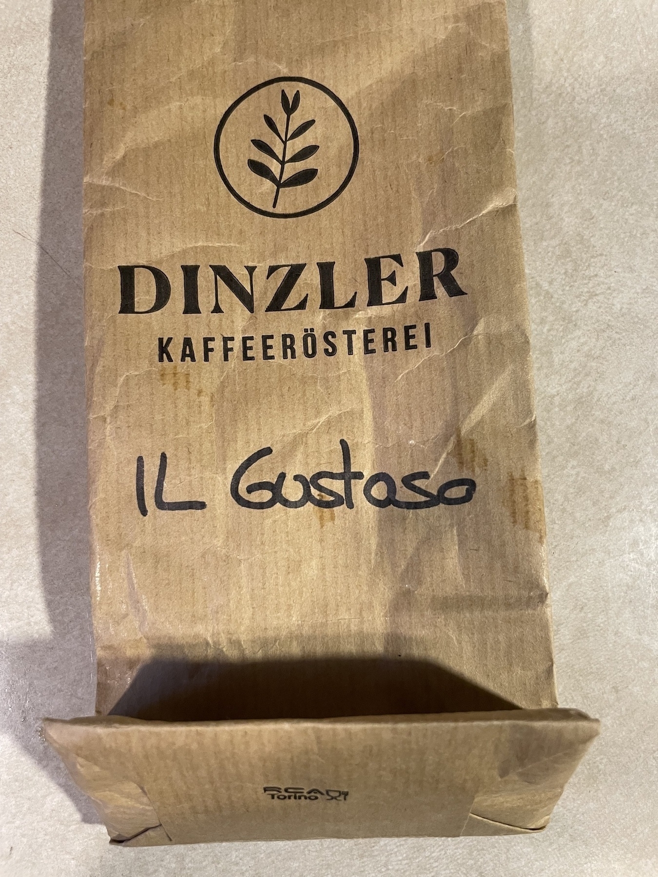 A brown paper coffee bag labeled "DINZLER KAFFEERÖSTEREI Il Gustoso" is lying on a surface.