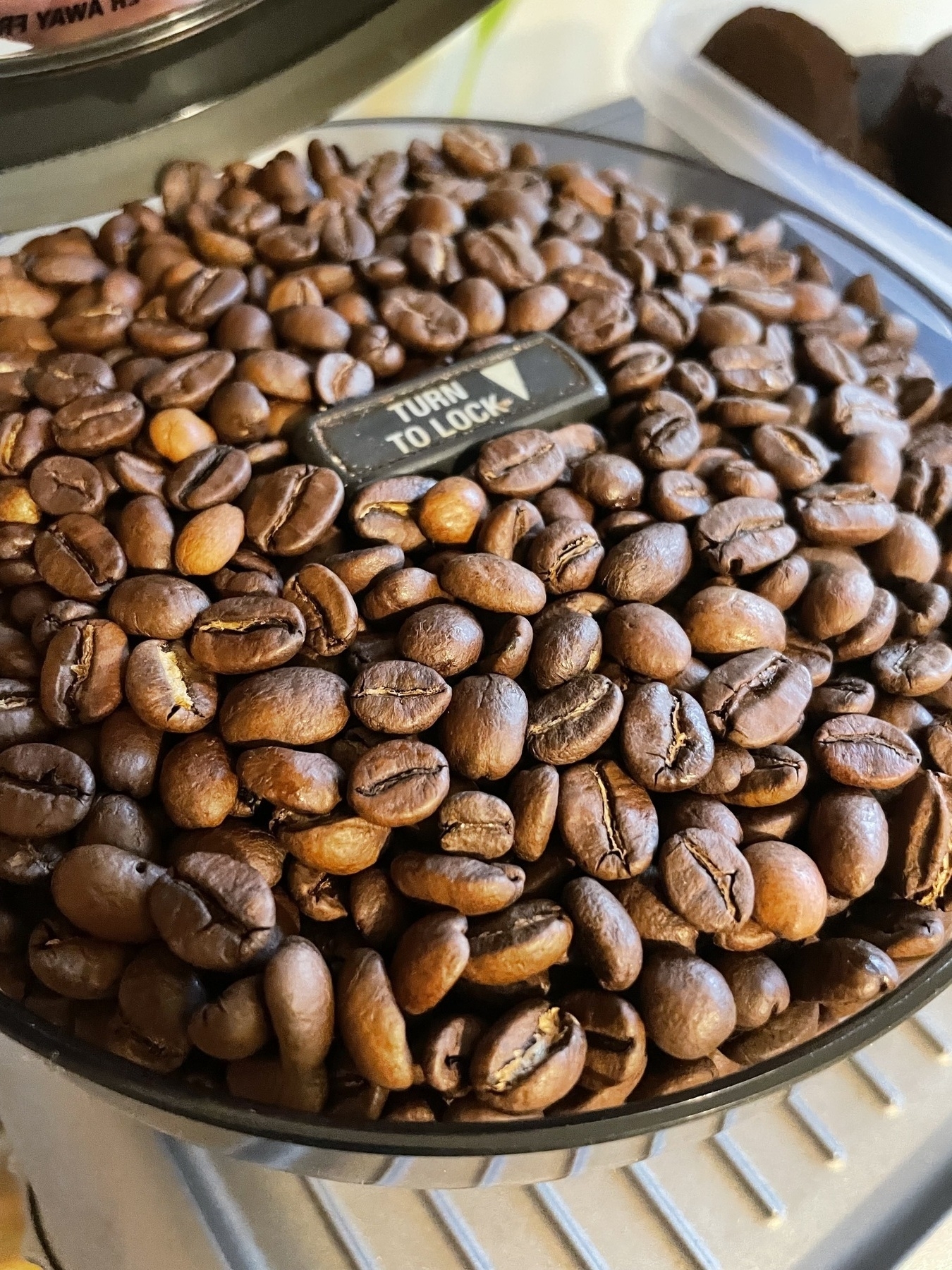 A container filled with roasted coffee beans, with a label instructing to "TURN TO LOCK" visible on top.
