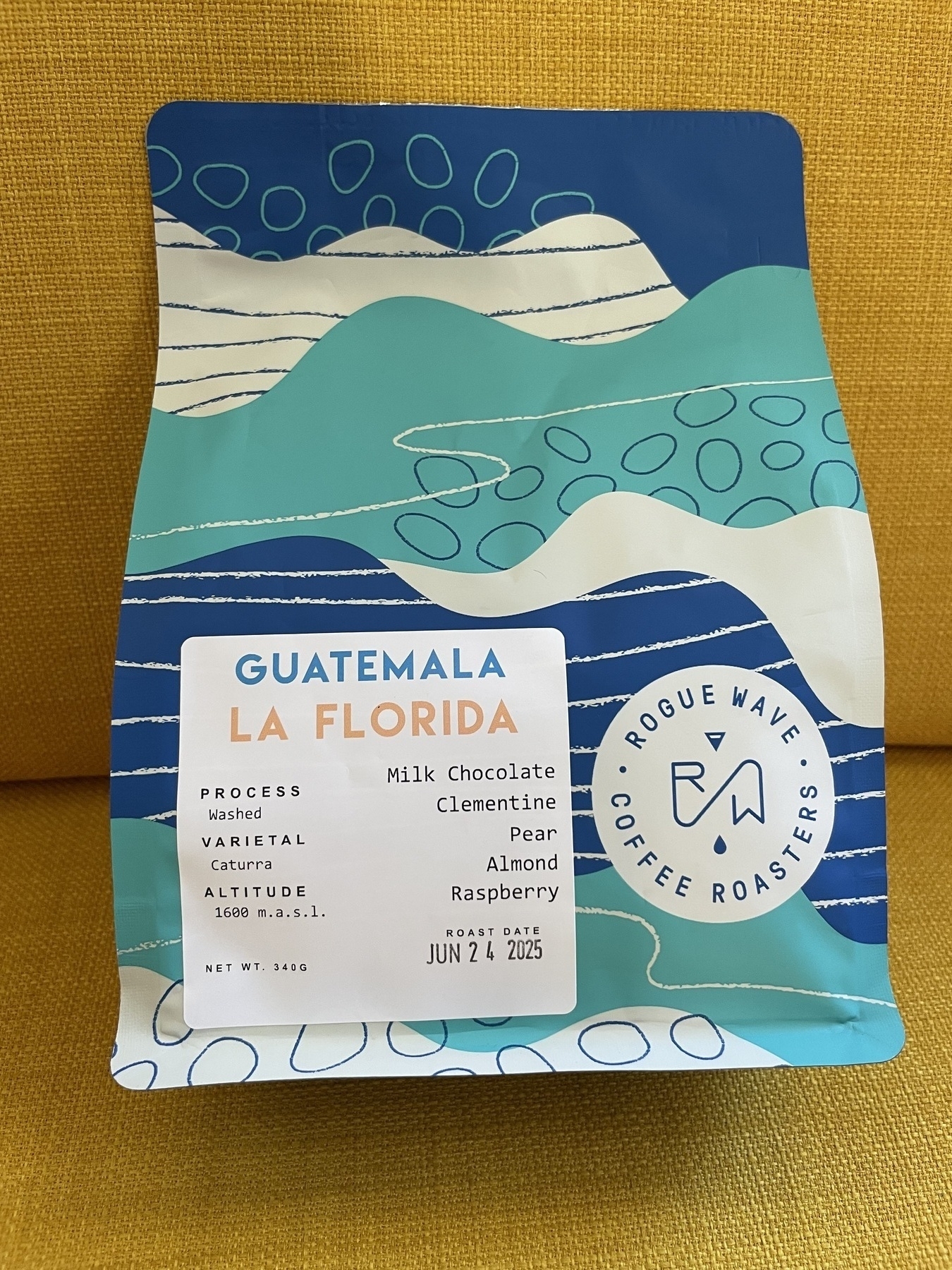 A colorful coffee bag from Rogue Wave Coffee Roasters labeled "Guatemala La Florida" includes tasting notes like milk chocolate, clementine, pear, almond, and raspberry.