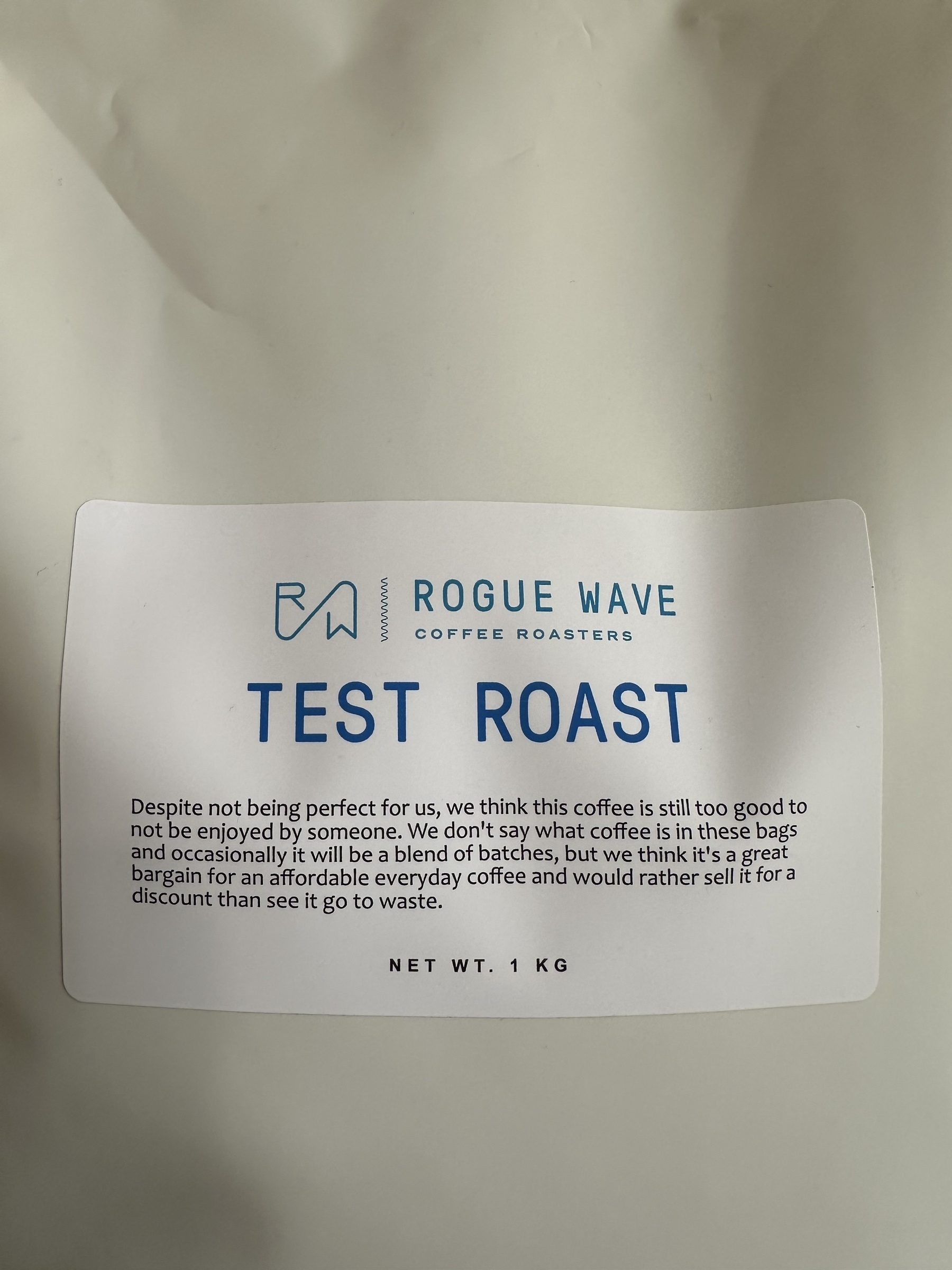 A labeled coffee bag from Rogue Wave Coffee Roasters suggests trying their test roast, described as a bargain despite imperfections, weighing 1 kg.