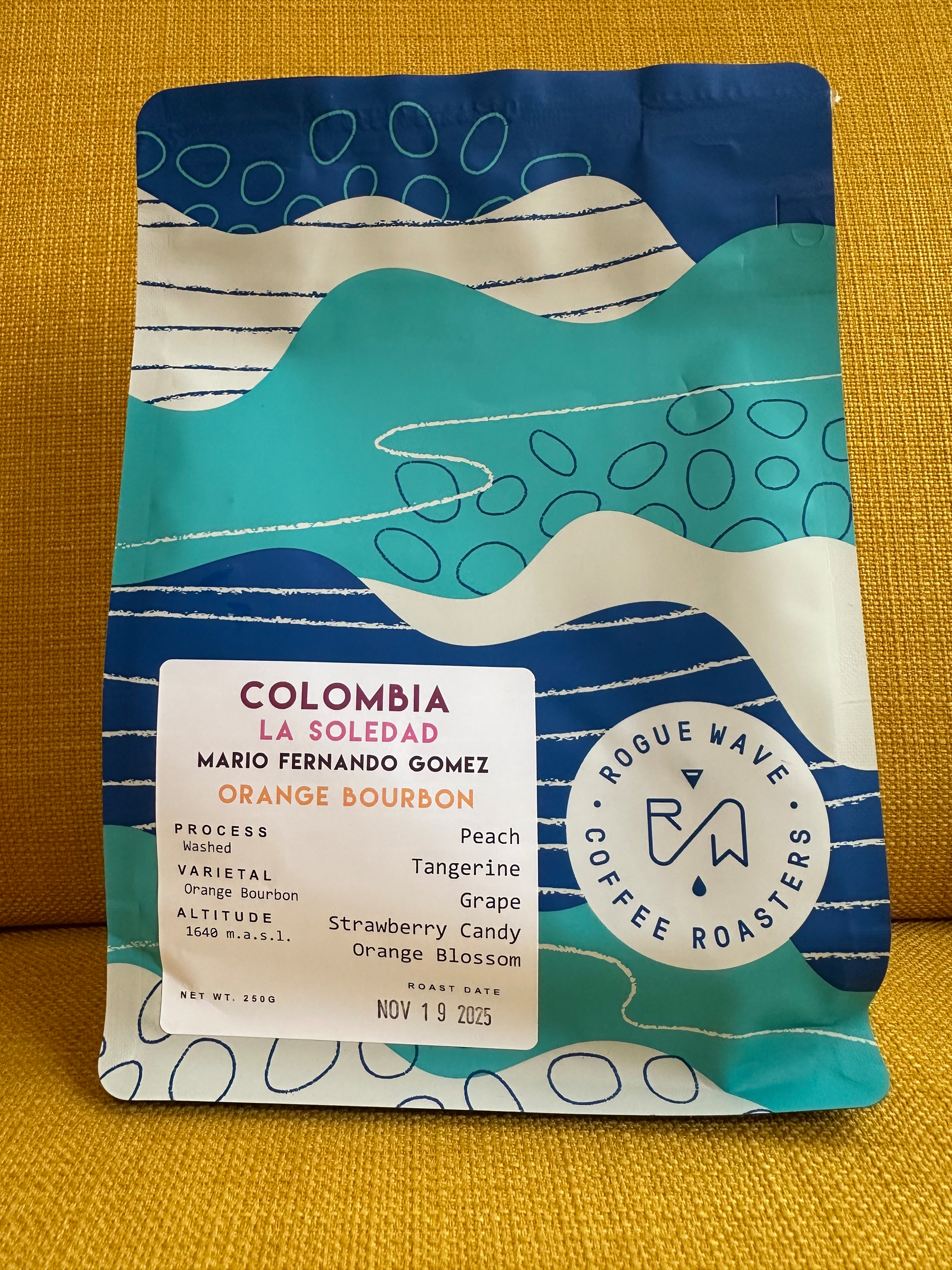 A colorful package of Rogue Wave Coffee Roasters' La Soledad Orange Bourbon coffee displays tasting notes like peach, tangerine, and grape.