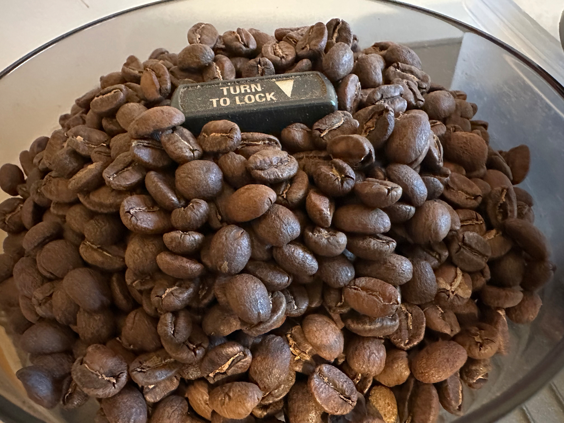 A container filled with roasted coffee beans features a black locking mechanism labeled TURN TO LOCK at the center.