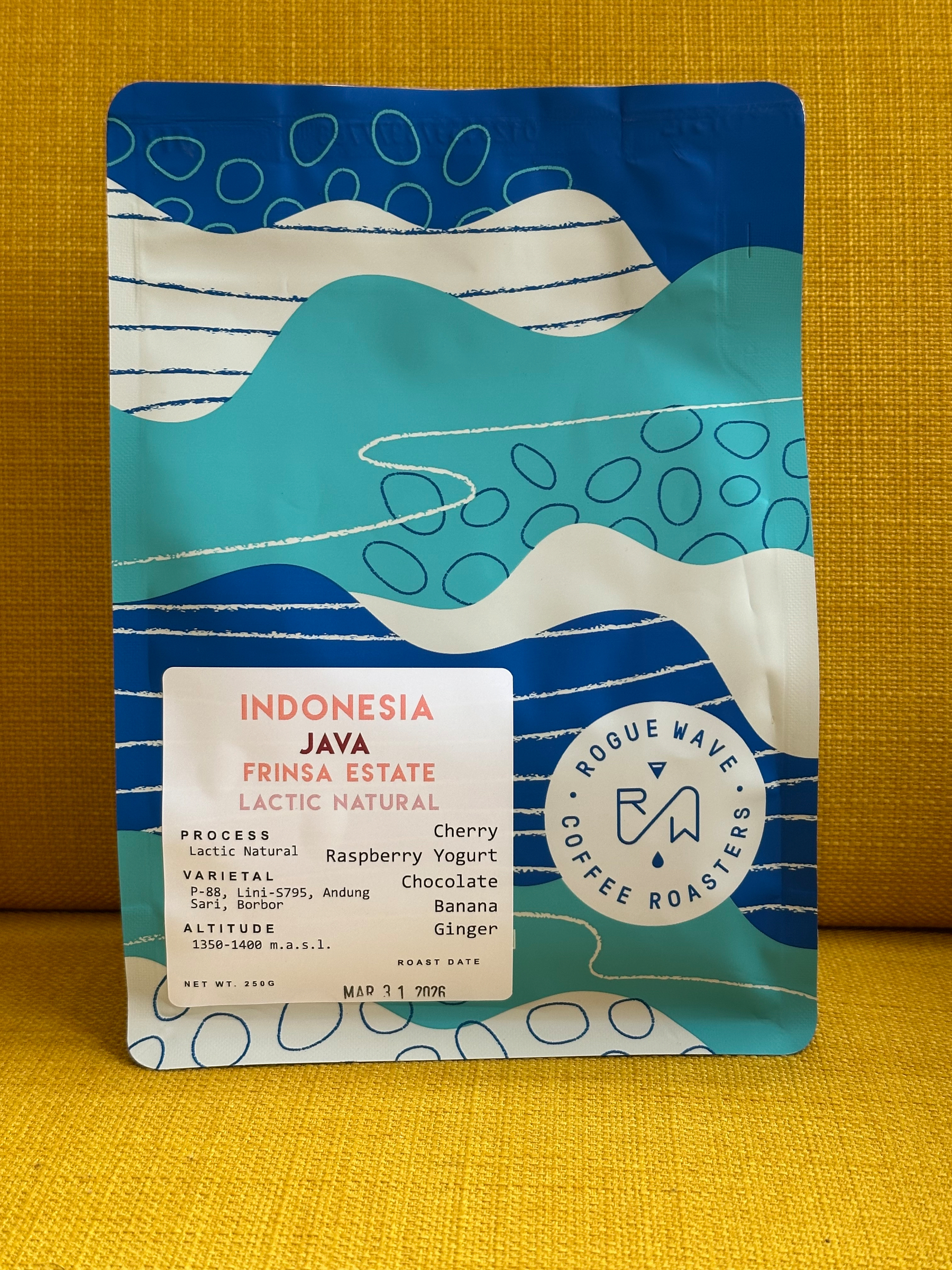 A colorful bag of Rogue Wave Coffee Roasters featuring Indonesia Java Frinsa Estate Lactic Natural coffee is displayed against a yellow background.