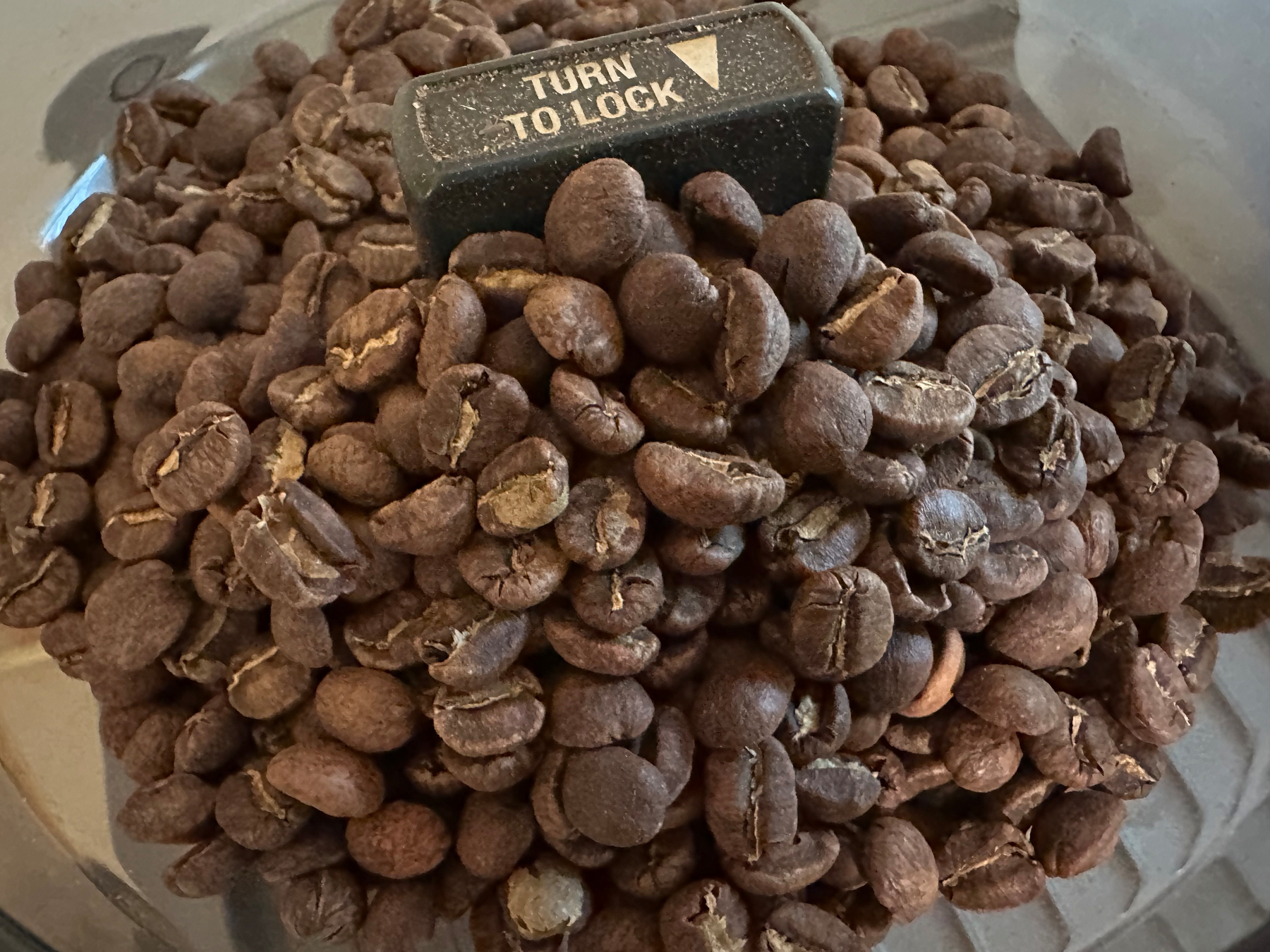 A pile of coffee beans is surrounding a TURN TO LOCK knob.