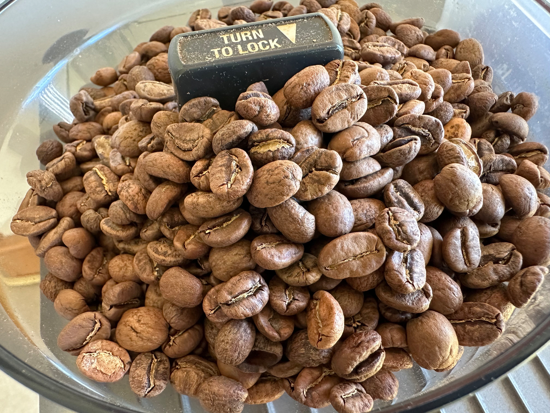 A pile of coffee beans is inside a container with a TURN TO LOCK mechanism on the lid.