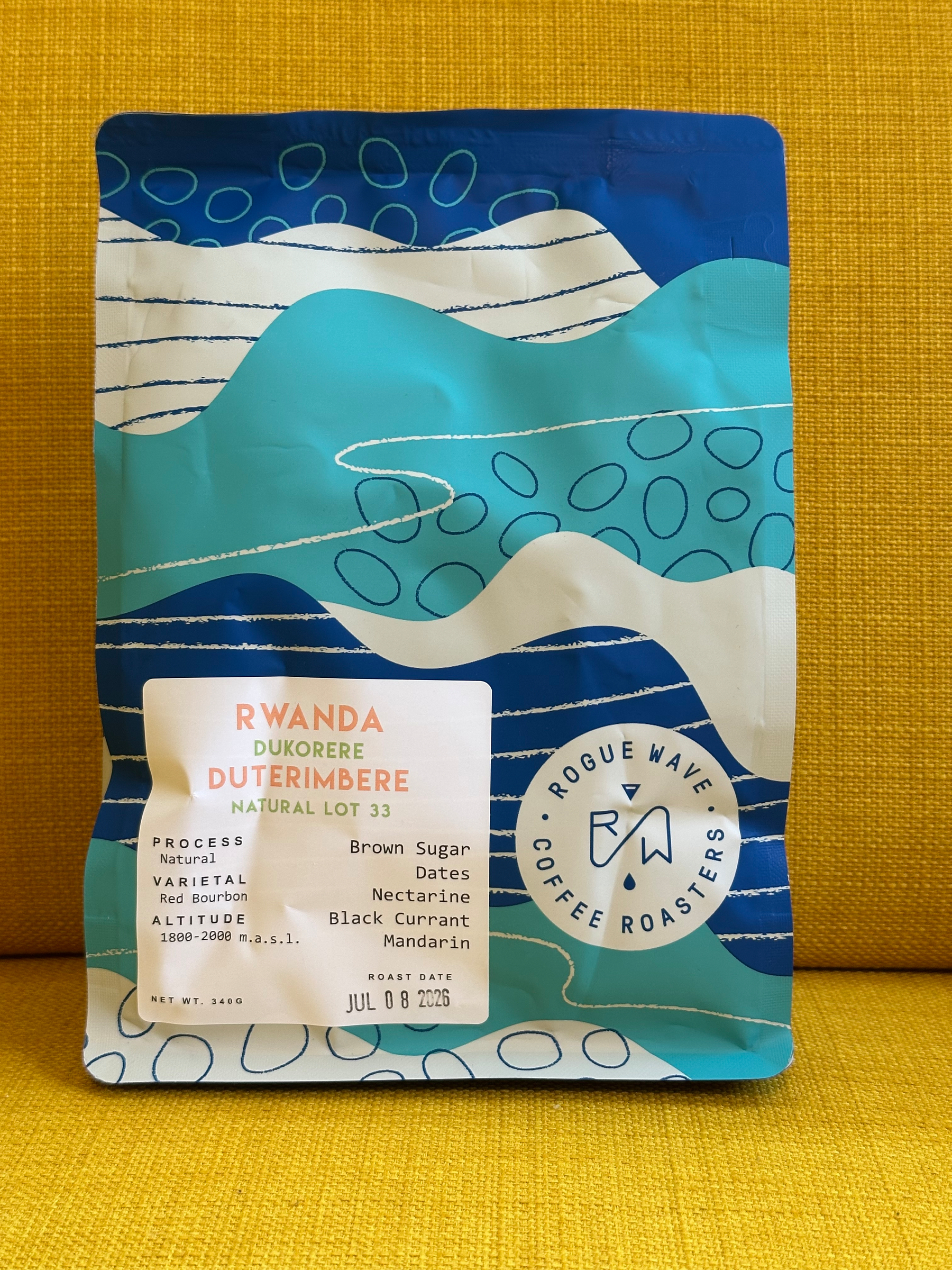 A colorful bag of Rogue Wave Coffee Roasters featuring Rwanda Dukorere Duterimbere natural lot 33 with tasting notes of brown sugar, dates, nectarine, black currant, and mandarin.