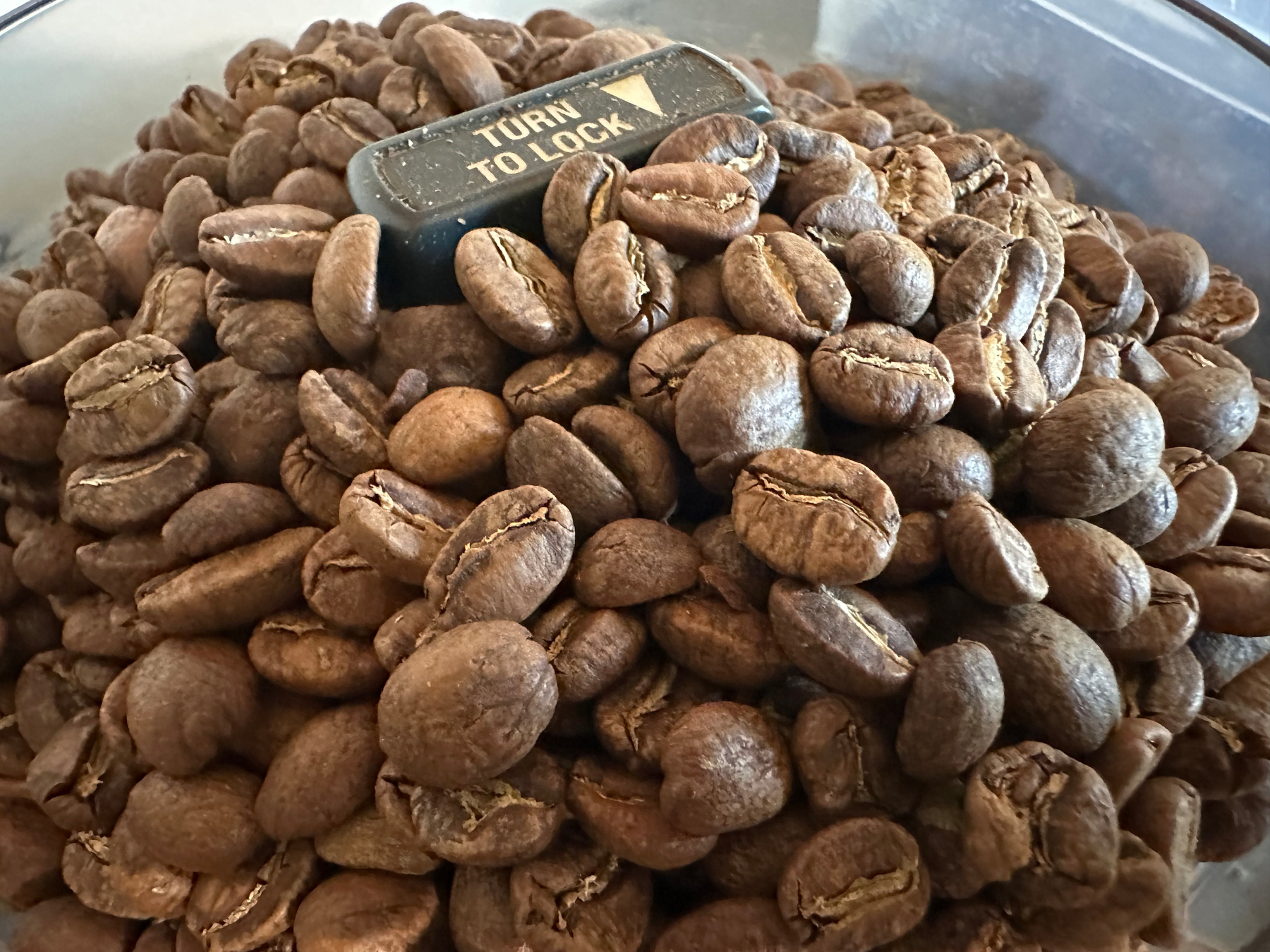 A container filled with roasted coffee beans and a small black knob labeled TURN TO LOCK is visible.
