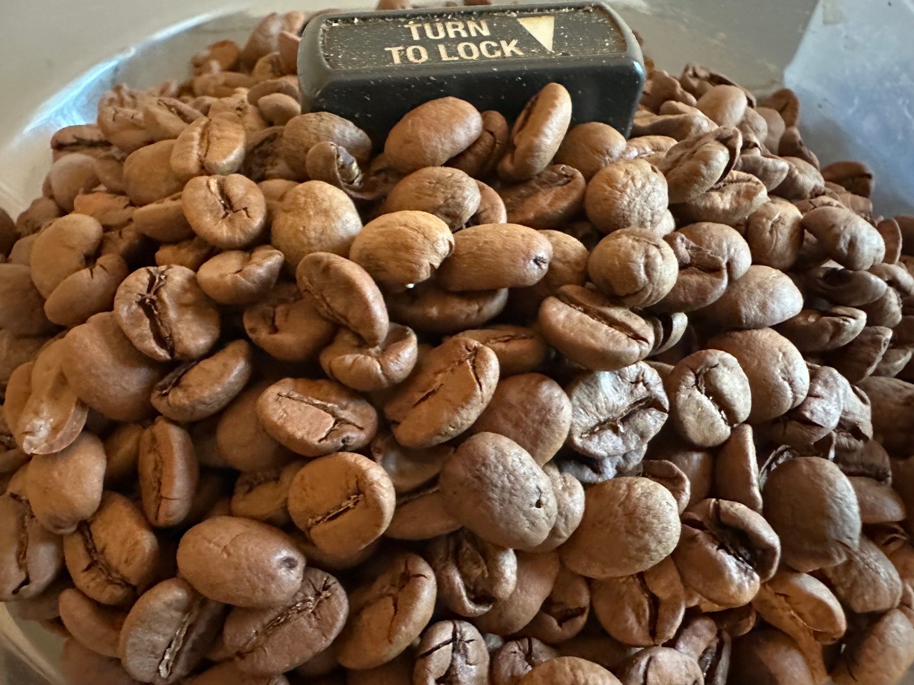A pile of roasted coffee beans surrounds a black knob with the words TURN TO LOCK printed on it.