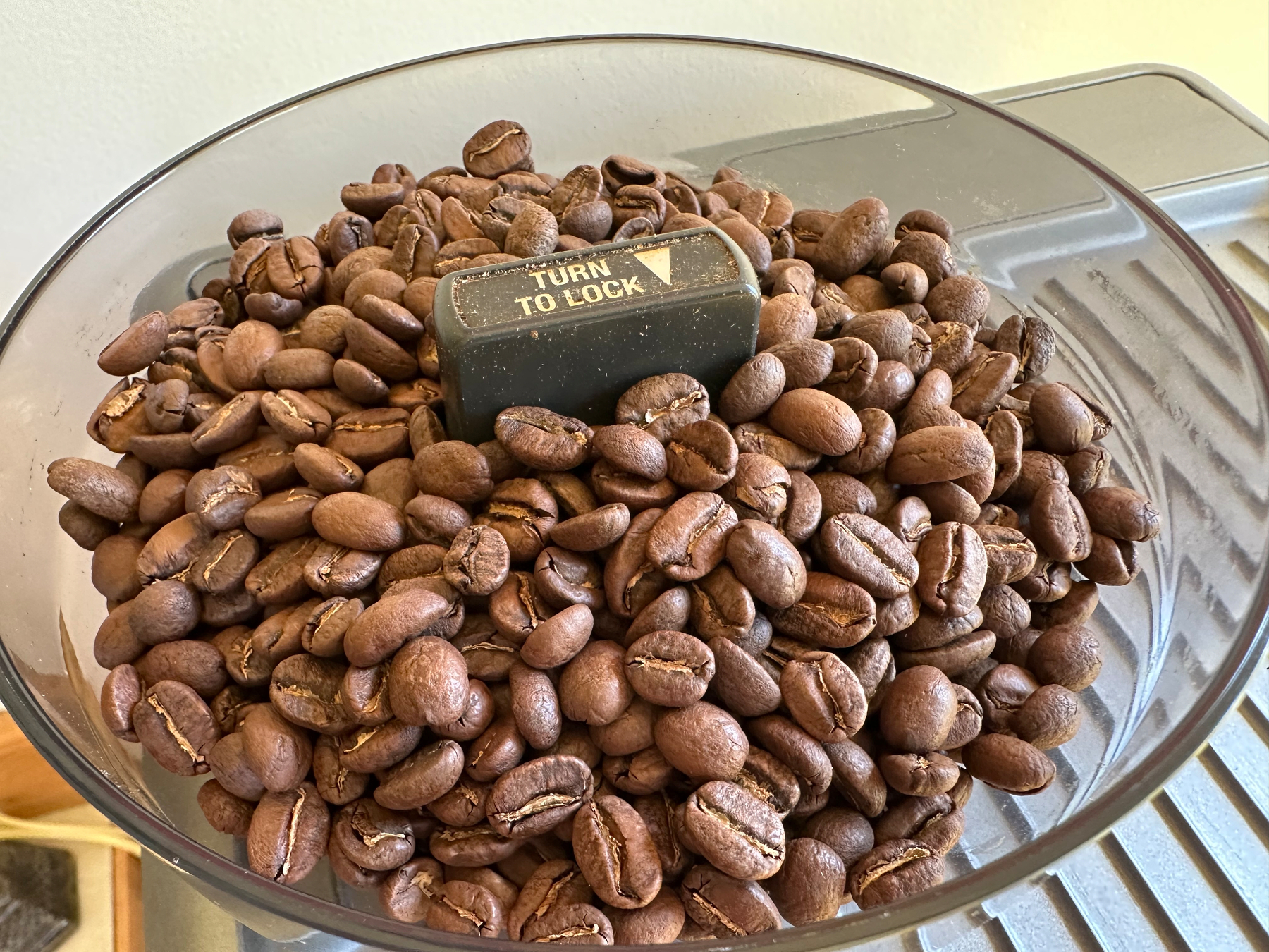 A container is filled with roasted coffee beans surrounding a black plastic piece labeled TURN TO LOCK.