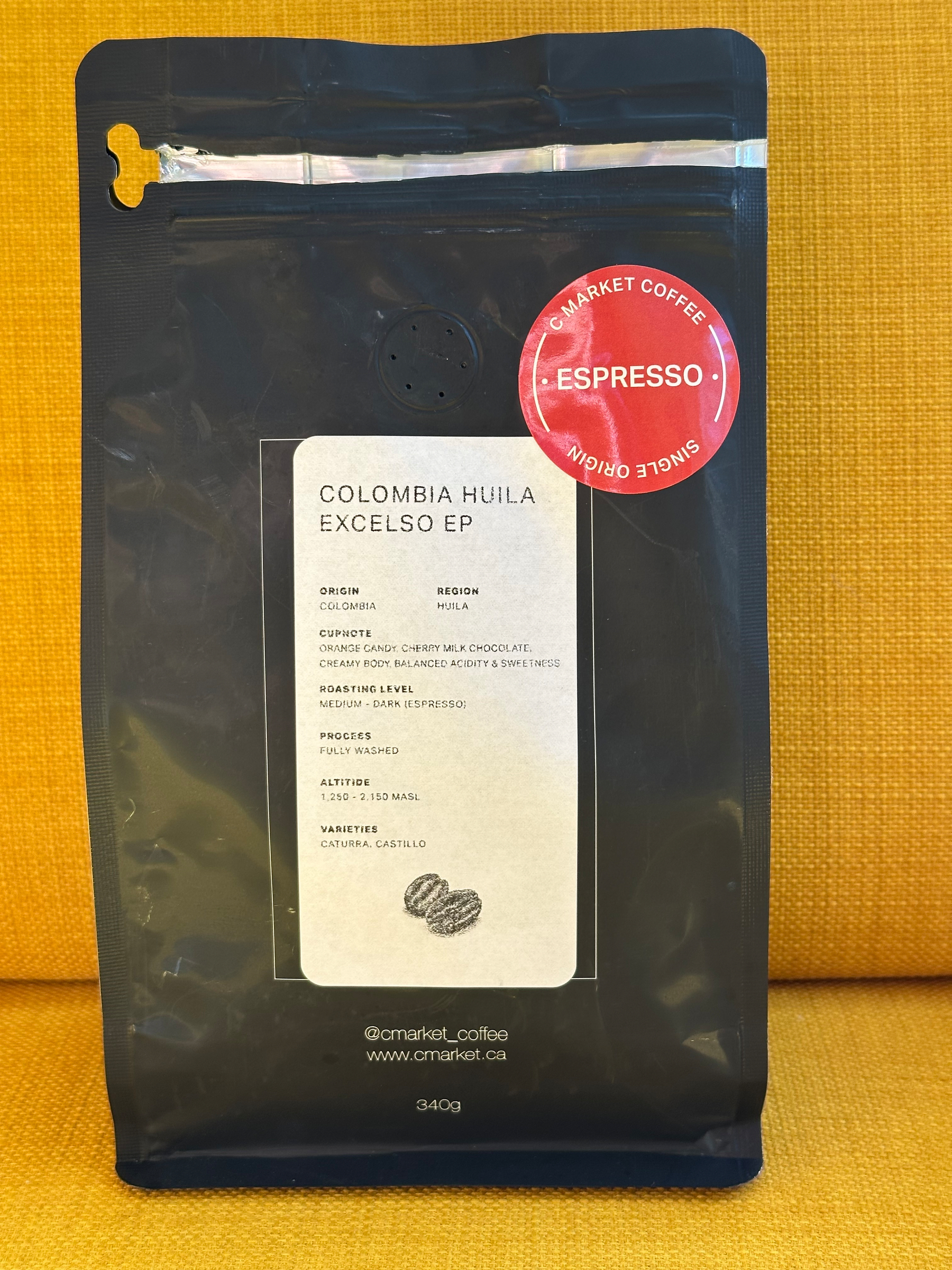 A 340g black bag of Colombia Huila Excelso EP espresso coffee from C Market Coffee, detailing its origin, cup notes, roasting level, process, altitude, and varieties.
