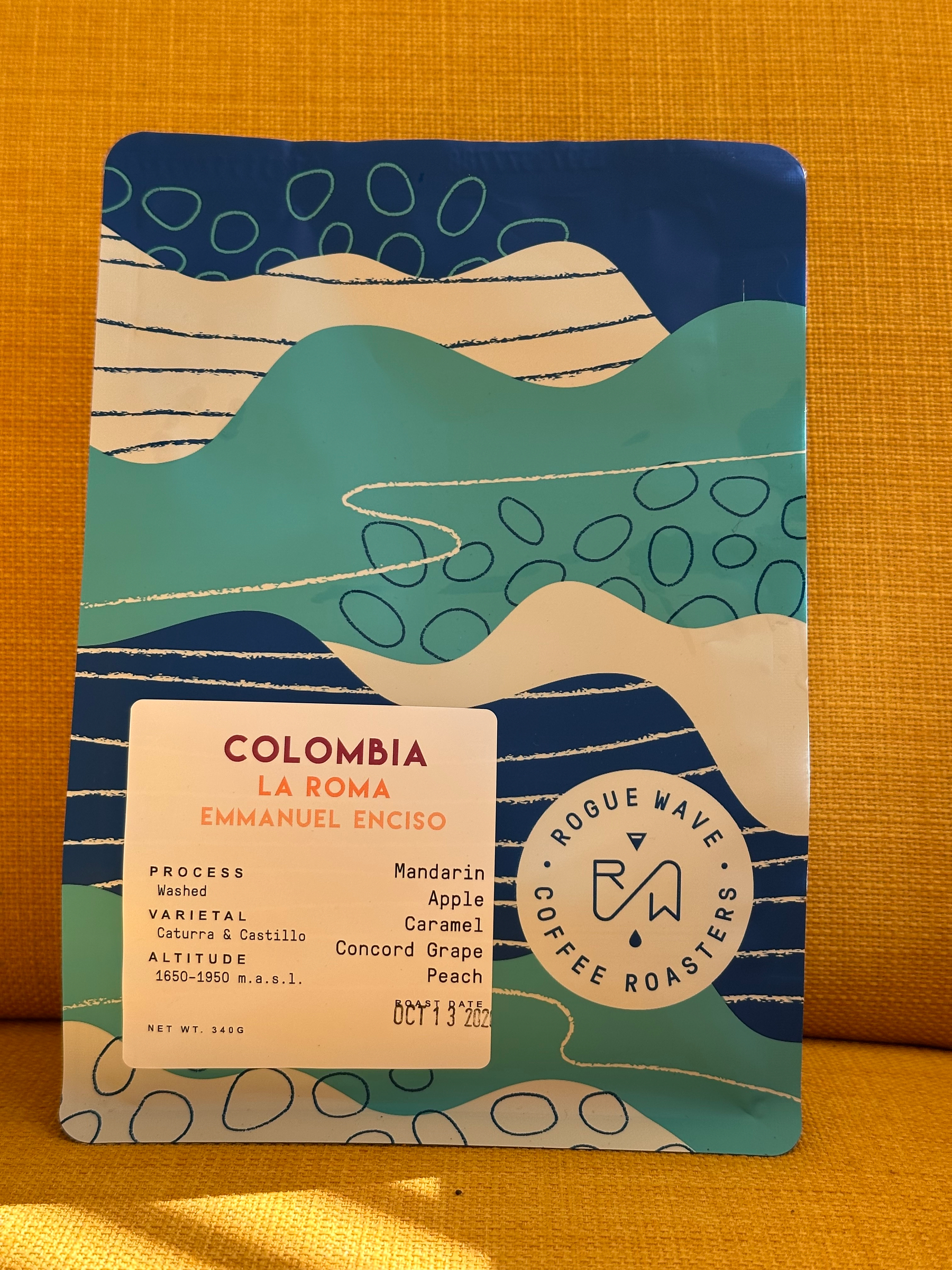 A colorful packaged bag of Rogue Wave Coffee Roasters features coffee from Colombia, La Roma, processed by Emmanuel Enciso with tasting notes of mandarin, apple, caramel, concord grape, and peach.
